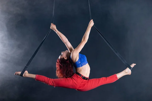 Weibliche athletische, sexy und flexible Zirkusartistin mit Rotschopf auf Antennenriemen auf schwarzem Hintergrund — Stockfoto