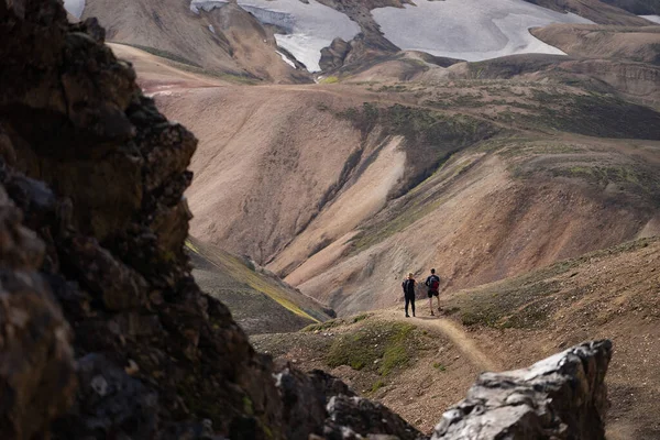 Серпень 2019. Долина Ландманналаугар. Ісландія. Два туриста в барвистих горах на трасі Логавегур. Поєднання шарів багатокольорових порід, мінералів, трави і моху. — стокове фото
