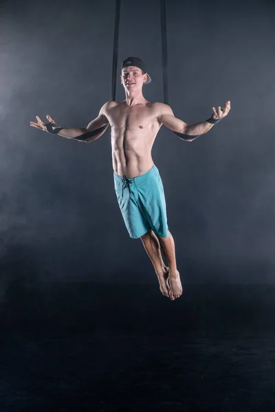 Circus kunstenaar op de antenne riemen met sterke spieren op zwarte achtergrond dragen casual kleding — Stockfoto