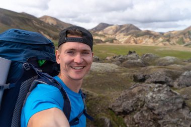 Sırt çantalı gezgin Landmannalaugar Vadisi 'nde selfie çekiyor. İzlanda. Laugavegur yürüyüş yolunda renkli dağlar. Çok renkli kaya, mineral, ot ve yosun katmanlarının birleşimi
