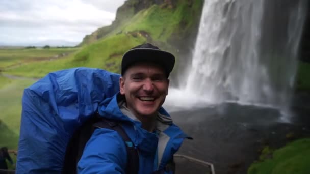 Turista feliz tomando selfie con hermosa cascada de Seljalandsfoss en el fondo. Concepto de viaje y estilo de vida saludable . — Vídeo de stock