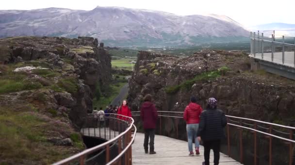 Iceland - July 2018: Many tourists walking on the lower trail sandwiched between the broken-apart cliffs at Thingvellir national park — Αρχείο Βίντεο