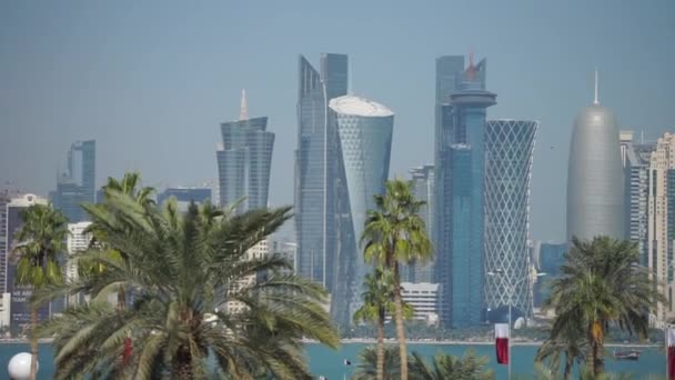 Панорамный вид на современные горизонты Дохи через размытые пальмы. Катар в солнечный день — стоковое видео