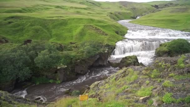 Bela cachoeira poderosa em câmera lenta cercada por colinas verdes durante o pôr do sol na trilha de caminhadas Fimmvorduhals perto de Skogar. Islândia — Vídeo de Stock