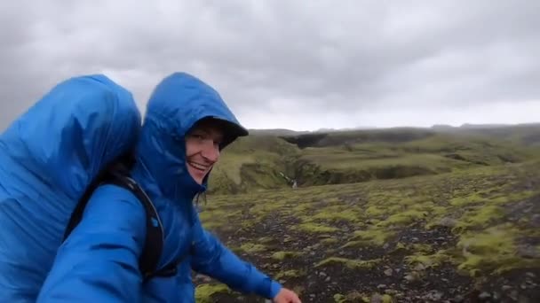 Glimlachende jongeman wandelt door ruw IJsland terrein bij sterke wind tot 30 wanten per seconde op de Fimmvorduhals wandelweg — Stockvideo