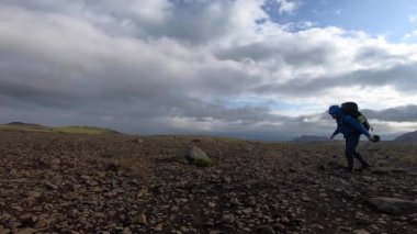 Genç adam, sert rüzgâr altında engebeli arazide yürür. Fimmvorduhals yürüyüş yolunda saniyede 30 km 'ye ulaşır.