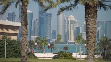 Doha 'nın modern ufuk çizgisinin bulanık palmiye ağaçları arasındaki panoramik görüntüsü. Güneşli günde Katar