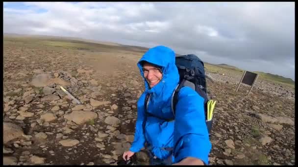 Gülümseyen genç adam zorlu İzlanda arazisinde yürürken Fimmvorduhals yürüyüş yolunda saniyede 30 mil hızla esiyor. — Stok video