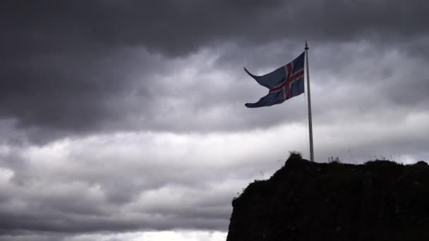Ісландський прапор на скелі в повільному русі з хмарною і вітряною погодою — стокове відео