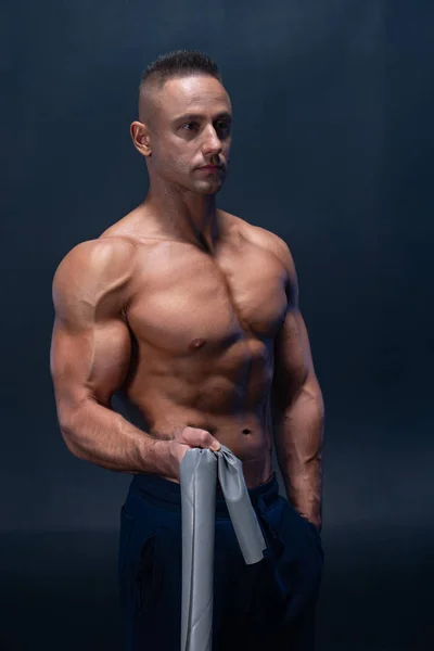 Muscular man doing calisthenic exercise with power band isolated on the black background — Stock Photo, Image