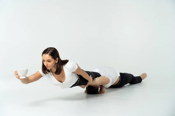 Chica bebiendo té durante Hurd truco acrobático con el hombre, aislado en blanco. Concepto de estilo de vida saludable y creatividad — Foto de Stock