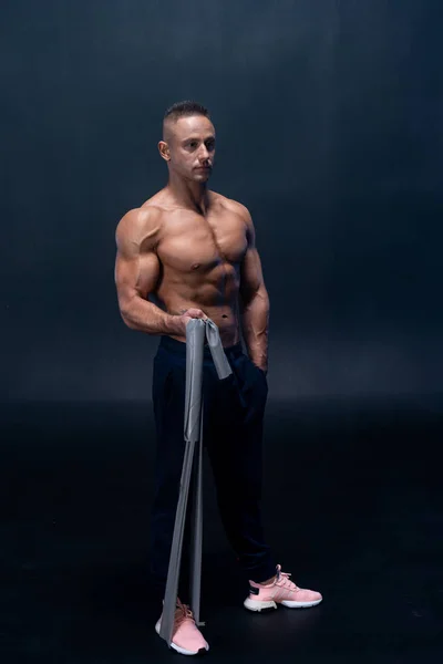 Hombre musculoso haciendo ejercicio calisténico con banda de potencia aislada sobre el fondo negro —  Fotos de Stock
