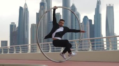 Cyr Wheel sanatçısı yavaş çekimde numaralar yapıyor. Gün batımında Dubai 'nin arka planında siyah beyaz kıyafetler giyiyor.