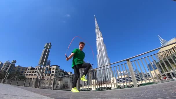 Hombre saltando con la cuerda de salto en el fondo del paisaje urbano de Dubai. Movimiento lento — Vídeos de Stock