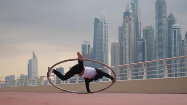 Cyr Wheel artista que usa ropa inteligente en blanco y negro con fondo de paisaje urbano de Dubai durante la puesta del sol — Vídeo de stock