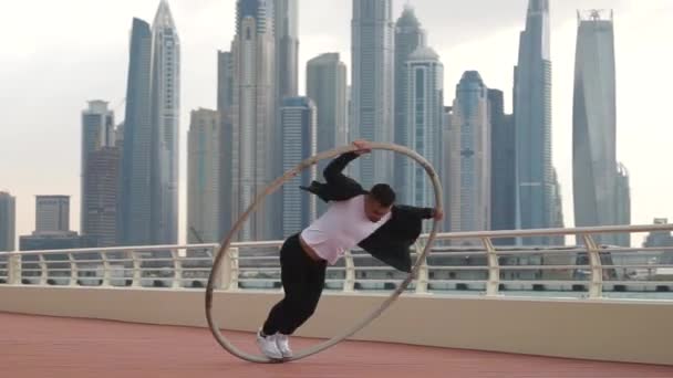 Cyr Wheel sanatçısı yavaş çekimde numaralar yapıyor. Gün batımında Dubai 'nin arka planında siyah beyaz kıyafetler giyiyor. — Stok video