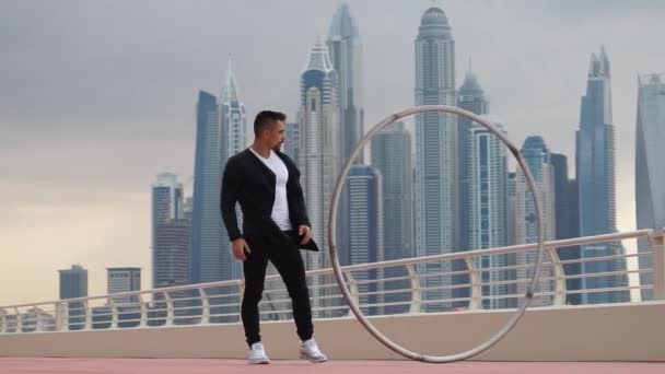 시어휠 아티스트가 해 가 지는 동안 두 바이의 도시 풍경을 배경으로 검고 하얀 옷을 입고 느린 동작을 하고 있다. — 비디오