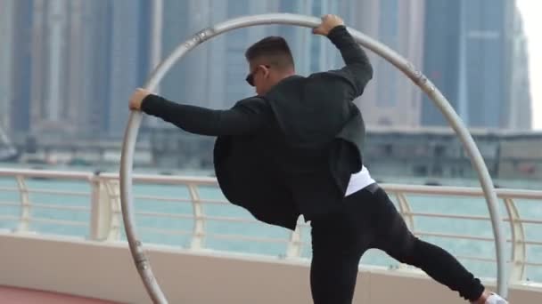 Cyr Wheel sanatçısı yavaş çekimde numaralar yapıyor. Gün batımında Dubai 'nin arka planında siyah beyaz kıyafetler giyiyor. — Stok video