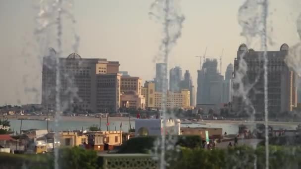 Unscharfe Ansicht einer Stadt mit Wasserfontänen in Zeitlupe im Vordergrund. Aufgenommen an einem sonnigen Tag, Doha, Katar — Stockvideo