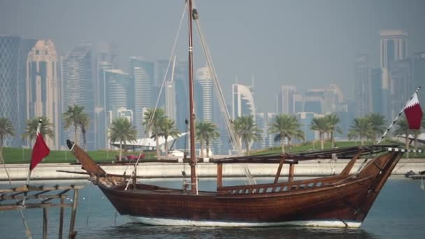 Ретро историческая лодка с размытым панорамным видом на современный горизонт Дохи и зеленые пальмы на заднем плане — стоковое видео