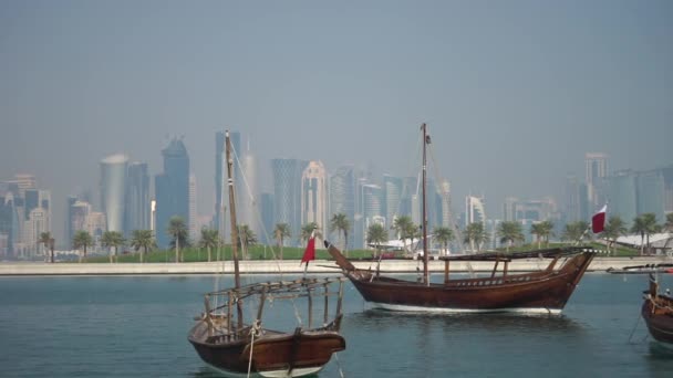 Ретро історичний човен з розмитим панорамним видом сучасного горизонту Доха і зелених пальм на задньому плані — стокове відео
