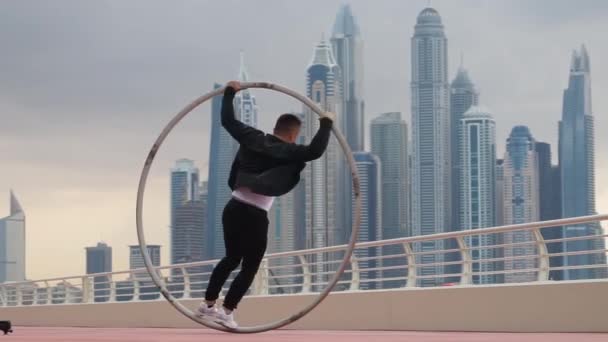 Cyr Wheel καλλιτέχνης κάνει κόλπα αργή κίνηση φορώντας μαύρο και άσπρο έξυπνα ρούχα με φόντο αστικό τοπίο του Ντουμπάι κατά τη διάρκεια του ηλιοβασιλέματος — Αρχείο Βίντεο