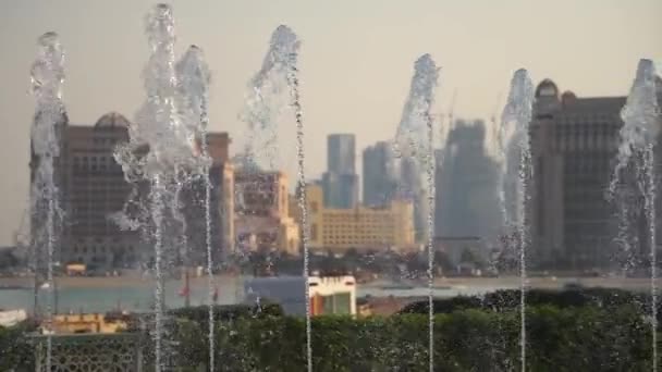 Rozmazaný pohled na město s pomalými fontánami v popředí. Je slunečný den, Dauhá, Katar — Stock video