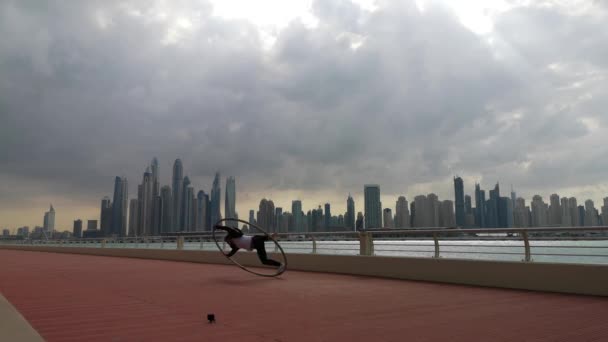 Cyr Wheel kunstenaar het dragen van zwart-wit slimme kleren met stadsgezicht achtergrond van Dubai tijdens zonsondergang — Stockvideo