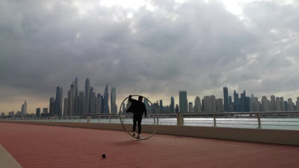 Cyr Wheel Künstler trägt schwarz-weiße smarte Kleidung mit Stadtbild Hintergrund von Dubai während des Sonnenuntergangs — Stockvideo