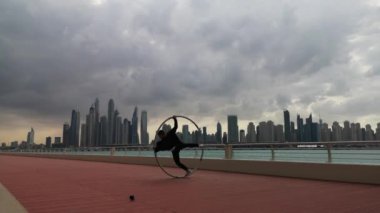 Günbatımında Dubai 'nin arka planında siyah beyaz şık kıyafetler giyen Cyr Wheel sanatçısı