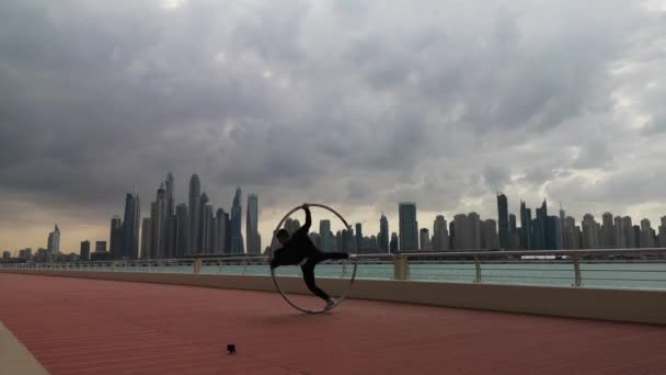 Cyr Wheel kunstenaar het dragen van zwart-wit slimme kleren met stadsgezicht achtergrond van Dubai tijdens zonsondergang — Stockvideo