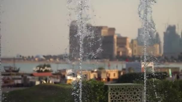 Vista turva de uma cidade com fontes de água em câmara lenta em primeiro plano. Tomado num dia ensolarado, Doha, Qatar — Vídeo de Stock
