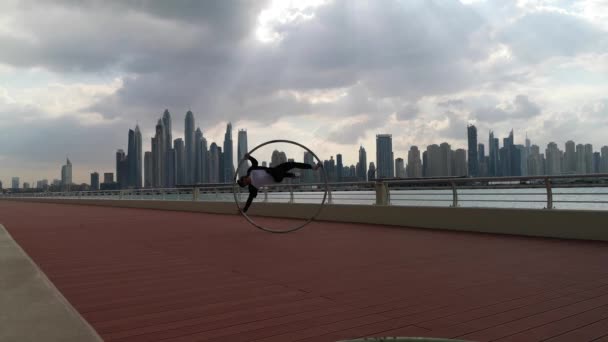 Cyr Wheel artista que usa ropa inteligente en blanco y negro con fondo de paisaje urbano de Dubai durante la puesta del sol — Vídeo de stock