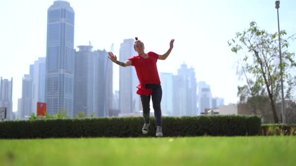 Mujer joven saltando acrobático de alto rendimiento en la hierba verde al aire libre en la ciudad de Dubai — Vídeos de Stock