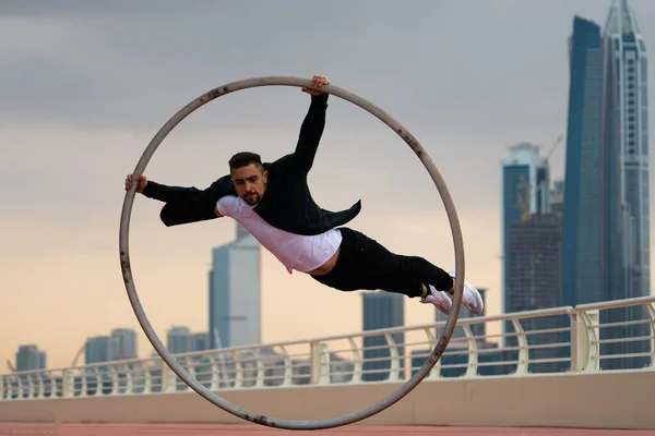 Cyr Wheel καλλιτέχνης φορώντας μαύρο και άσπρο έξυπνα ρούχα με φόντο αστικό τοπίο του Ντουμπάι κατά τη διάρκεια του ηλιοβασιλέματος — Φωτογραφία Αρχείου