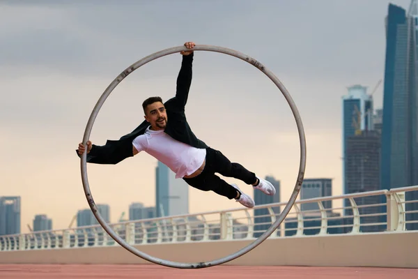 Cyr Wheel καλλιτέχνης φορώντας μαύρο και άσπρο έξυπνα ρούχα με φόντο αστικό τοπίο του Ντουμπάι κατά τη διάρκεια του ηλιοβασιλέματος — Φωτογραφία Αρχείου