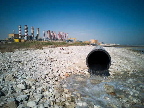 Close Up of Waste Waters Draining from Pipe with huge factory with lots of pipe on background