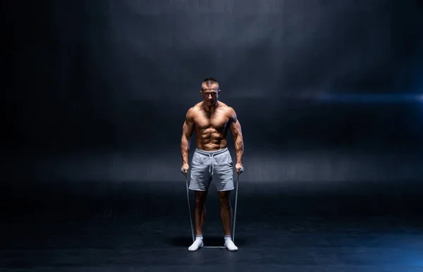 Homem muscular fazendo exercício calistênico com banda de força isolada no fundo preto — Fotografia de Stock