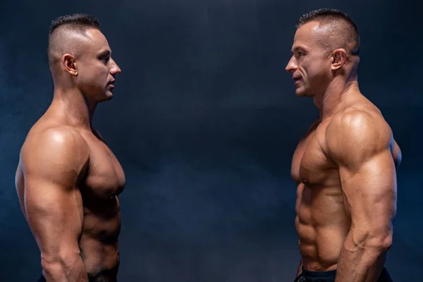 Dois homens musculosos em pé um contra o outro isolados no fundo preto. Conceito de confronto e luta — Fotografia de Stock