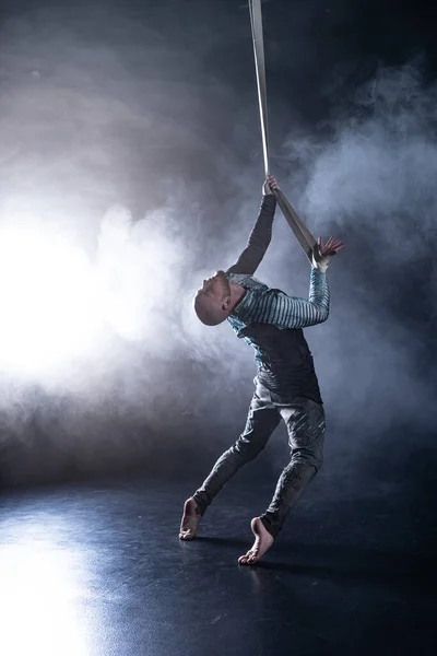 Artista de circo en las correas aéreas con traje en el fondo negro y ahumado. Concepto de sufrimiento, desesperación y derrota — Foto de Stock