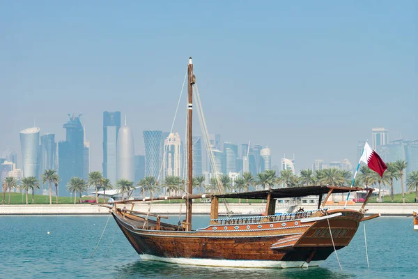 Retro historical boat with blurred panoramic view of modern skyline of Doha and green palms on background — Stock Photo, Image
