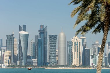 Doha 'nın modern ufuk çizgisinin bulanık palmiye ağaçları arasındaki panoramik görüntüsü. Güneşli günde Katar