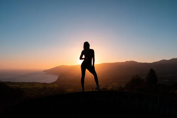 Silueta de mujer disfrutando de la libertad sintiéndose feliz al atardecer con montañas y mar sobre fondo — Foto de Stock