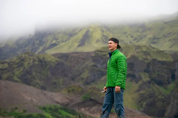 Backside of tall caucasian man wearing green jacket standing in over mountain and fog background. Promoting healthy lifestyle