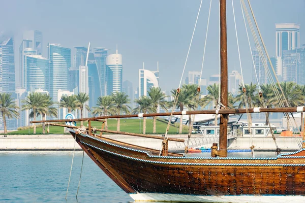 Retro historische boot met wazig panoramisch uitzicht op de moderne skyline van Doha en groene palmen op de achtergrond — Stockfoto