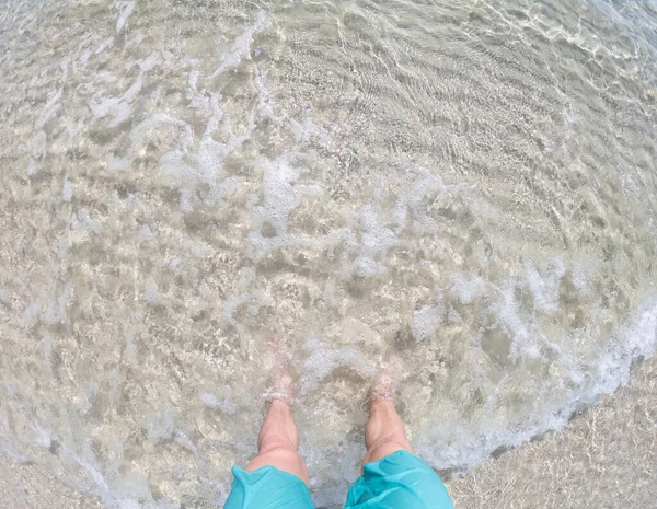 Manliga fötter står på den grunda kristallen Sea Water Beach Sand. Begreppet relsx och lycka. — Stockfoto