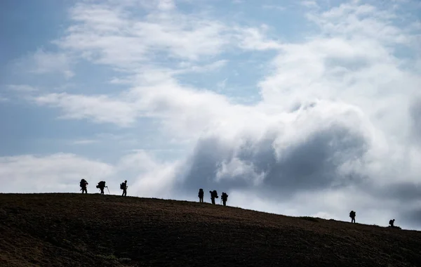 Silhouettes of people walking with backpacks on the sky background