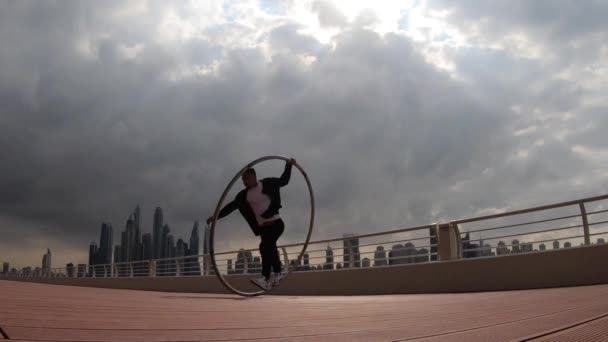 Cyr Wheel Künstler trägt schwarz-weiße smarte Kleidung mit Stadtbild Hintergrund von Dubai während des Sonnenuntergangs — Stockvideo