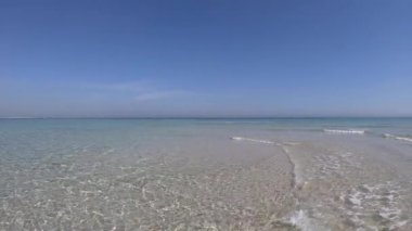 Kristal berrak sığ su ve mavi gökyüzü ile beyaz kum ağır çekim