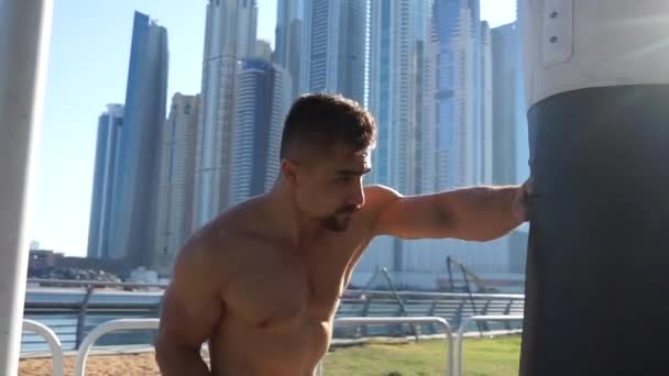 Hombre muscular golpeando saco de boxeo con paisaje urbano de Dubai en el fondo — Vídeo de stock